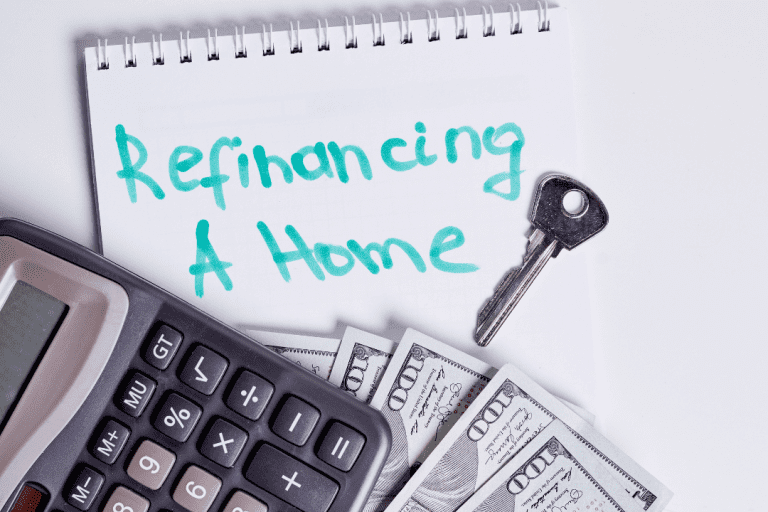 A calculator, cash, key and a notebook with the word ‘refinancing a home’ written
