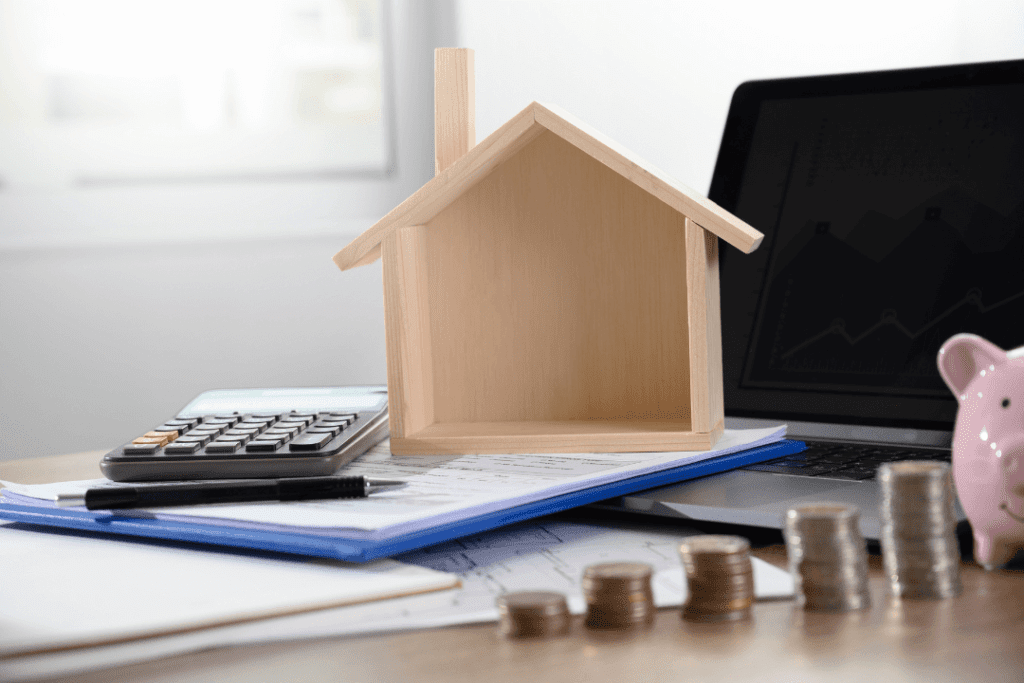 Image of a wooden block house on a desk with a calculator and some coins, to depict increasing home loan interest rates in Singapore