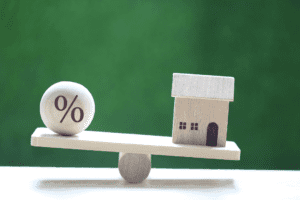 Image of a wooden block house and % sign on a see-saw, symbolising the balance between home loan interest rates in Singapore and inflation